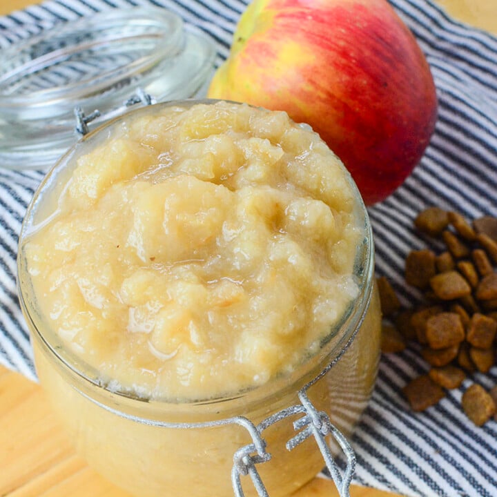 Finished applesauce in a glass container. On the right is a small bundle of kibble with an apple sitting at the top of the photo.