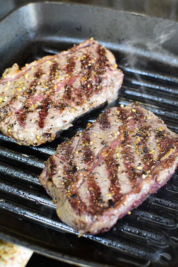 Flat iron steaks searing in a cast iron grill pan.