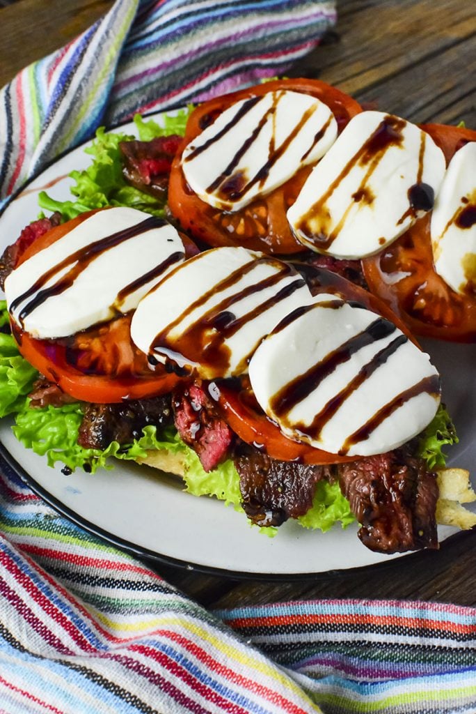 The open faced calabrese steak sandwiches sitting on a white enamel plate with a colorful napkin in the background.