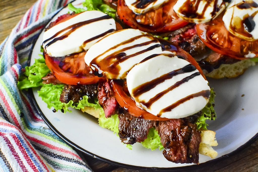 One of the caprese sandwiches shown upclose with a colorful napkin on the left of the plate.