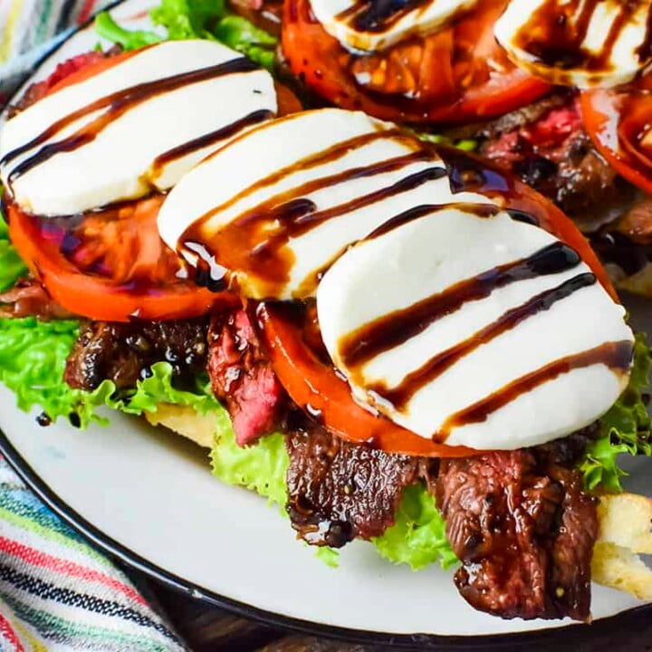 One of the caprese sandwiches shown upclose with a colorful napkin on the left of the plate.