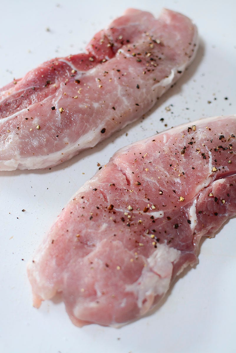 Raw pork steaks seasoned with salt and pepper. 