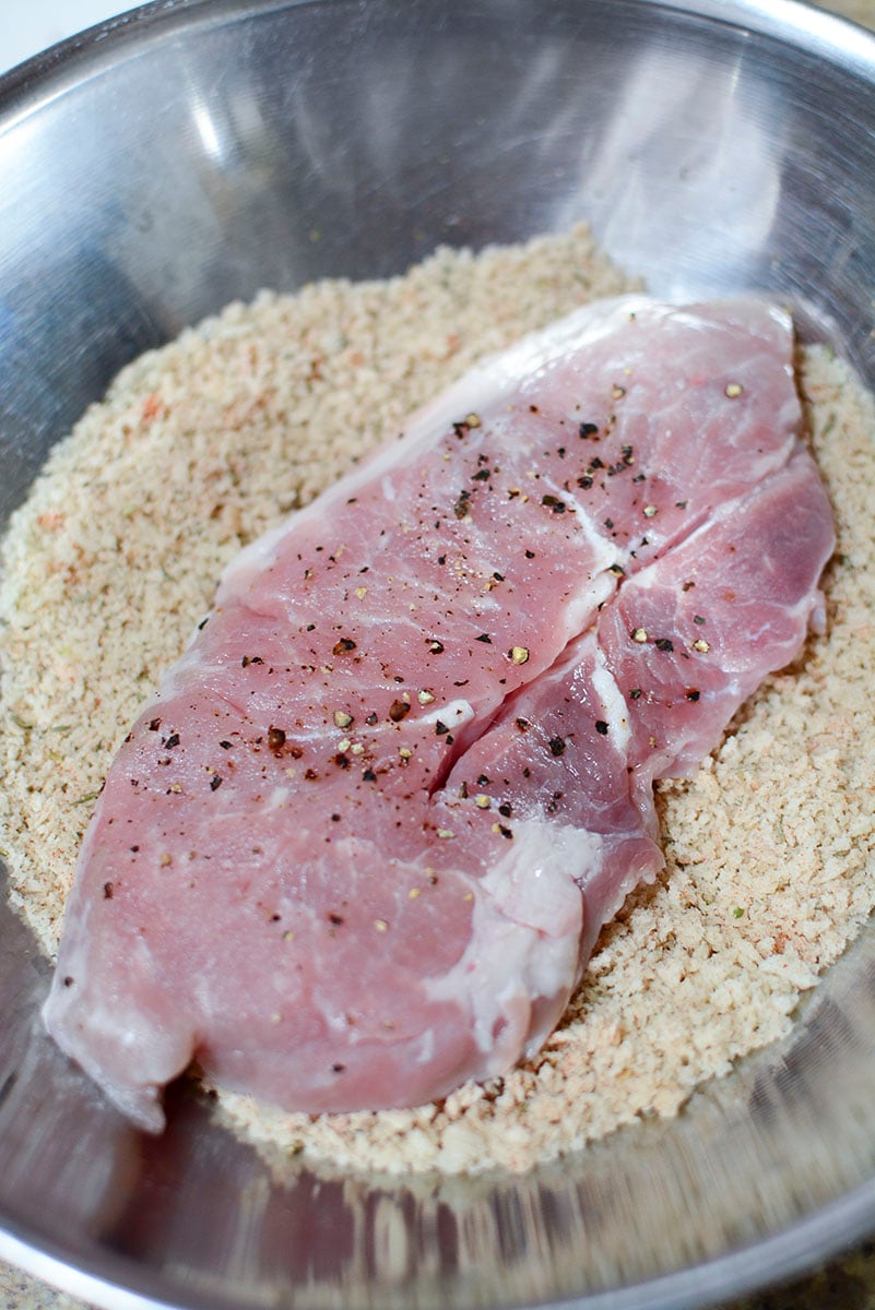 A pork steak being dredged in seasoned bread crumbs.