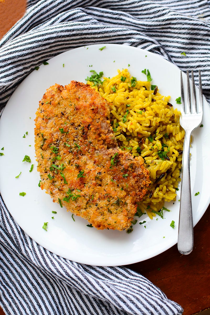 An air fried pork steak next to a bed of seasoned rice on a white plate.