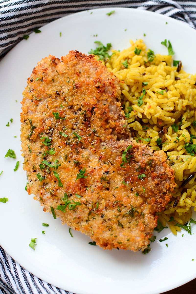 An air fried pork steak on a white plate with seasoned rice next to it.