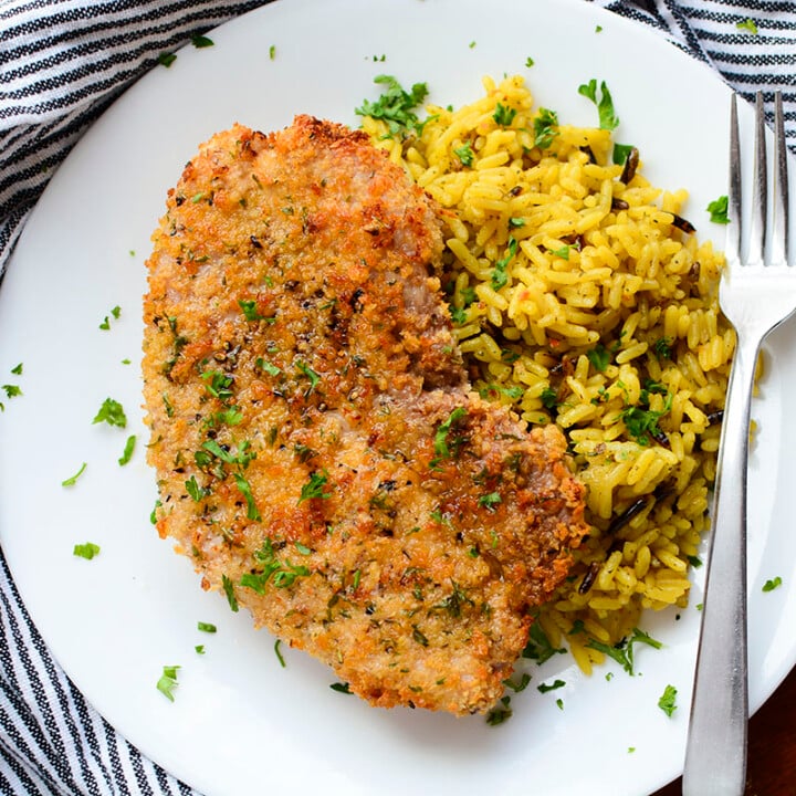 Air fryer pork steak next to a side of rice on a white plate. There is a fork on the right side of the plate.