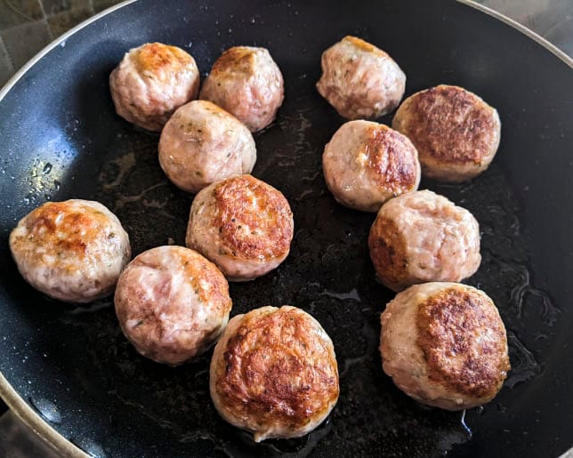 Sausage meatballs being seared in a skillet.
