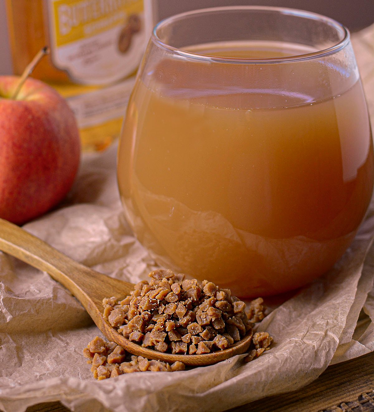 A large glass of toffee apple cider with a spoon full of toffee bits in front of the glass.