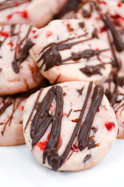 Shortbread cookies with cherries and chocolate piled together on a white plate.