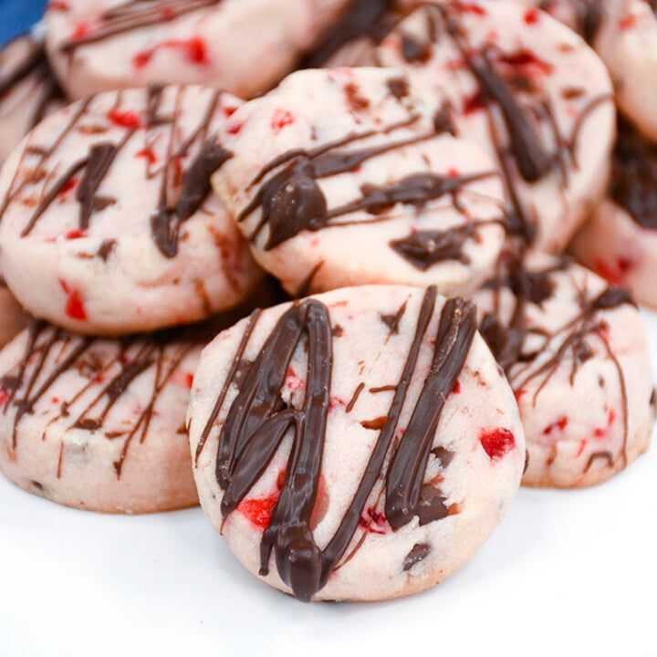 Shortbread cookies with cherries and chocolate piled together on a white plate.