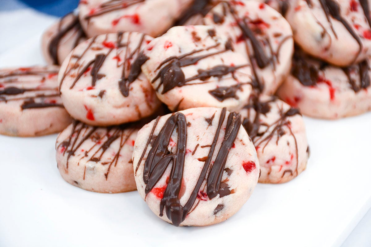 Shortbread cookies with cherries and chocolate piled together on a white plate.