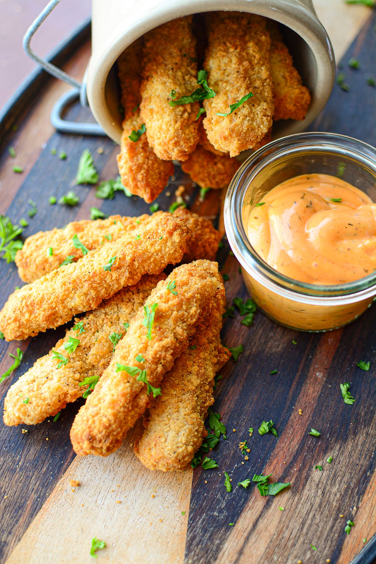 An order of chicken fries on a board with spicy dip on the side.