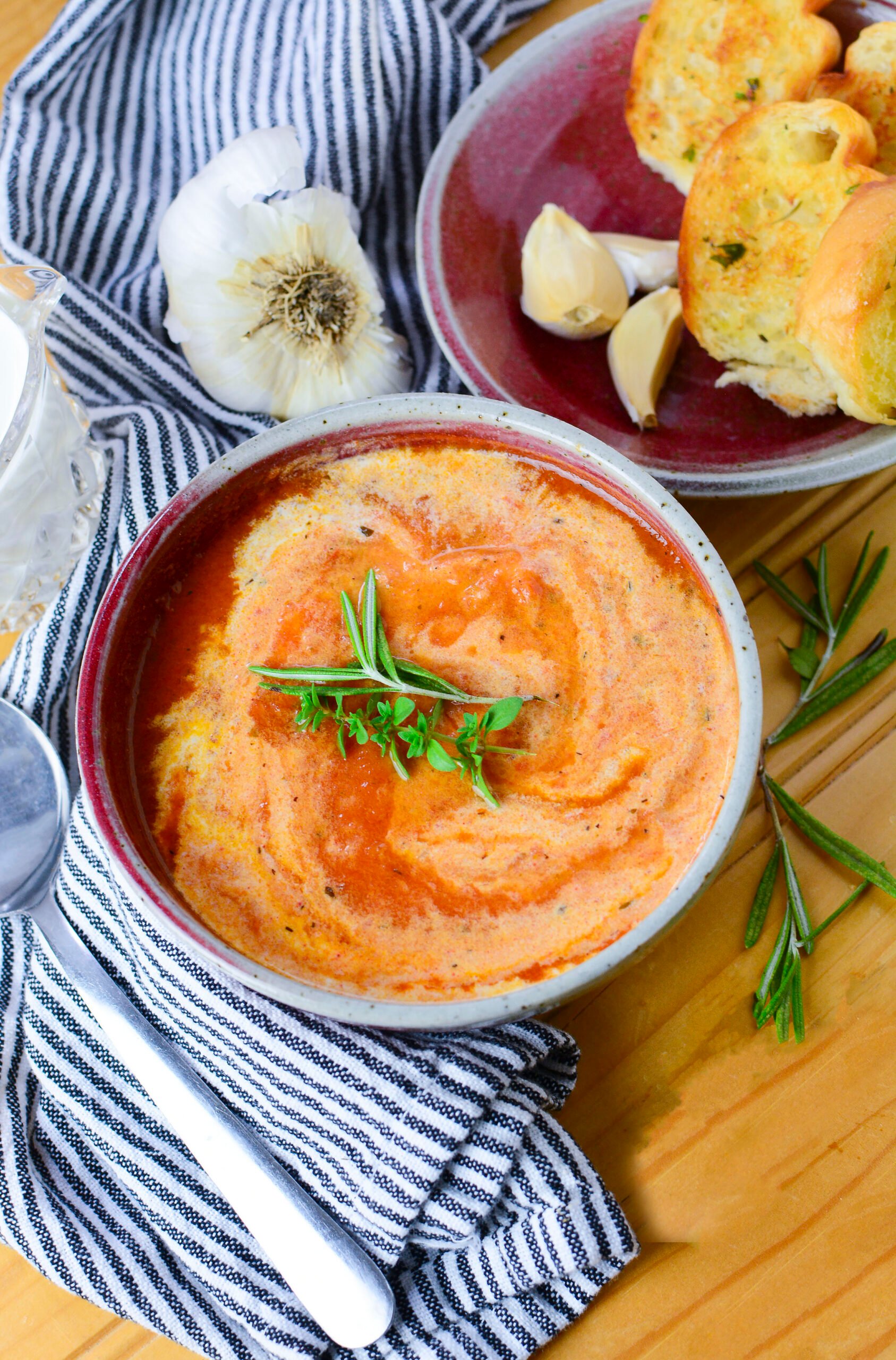 Soup in a red soup bowl with a striped black and white napkin around it.