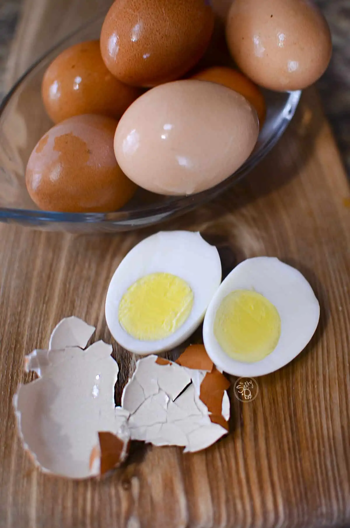 Hard boiled eggs in a glass boil at the top with one cooked egg split open and the shell on the left of it.