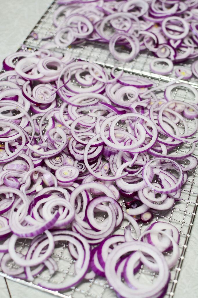 Sliced purple onions on metal trays ready to be dried.