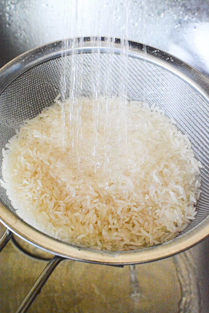 Rice in a metal sieve being washed. 