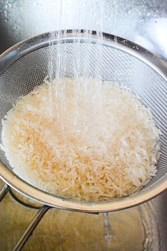 Rice in a metal sieve being washed. 