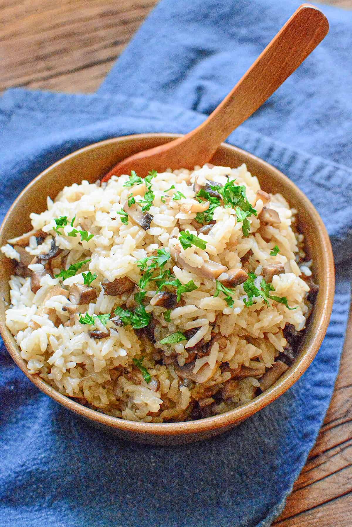Rice in a brown bowl with a wooden spoon sticking out of it.