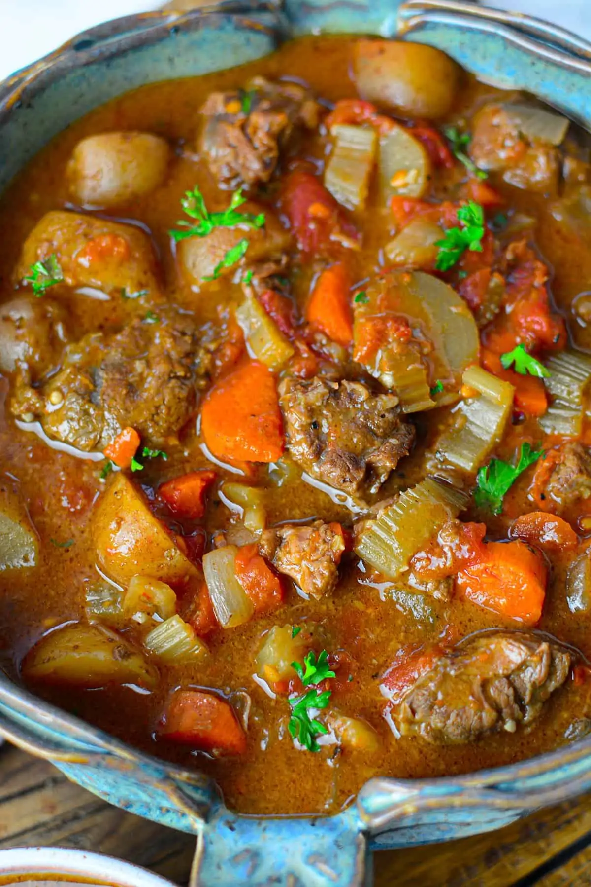 Beef stew in a blue bowl on a wooden board background.