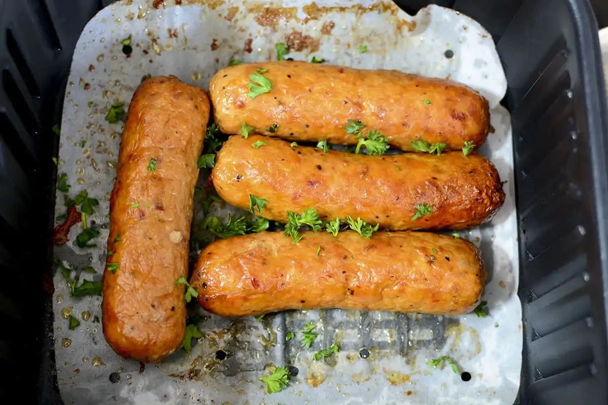 4 crispy air fryer chicken sausages in the air fryer basket.