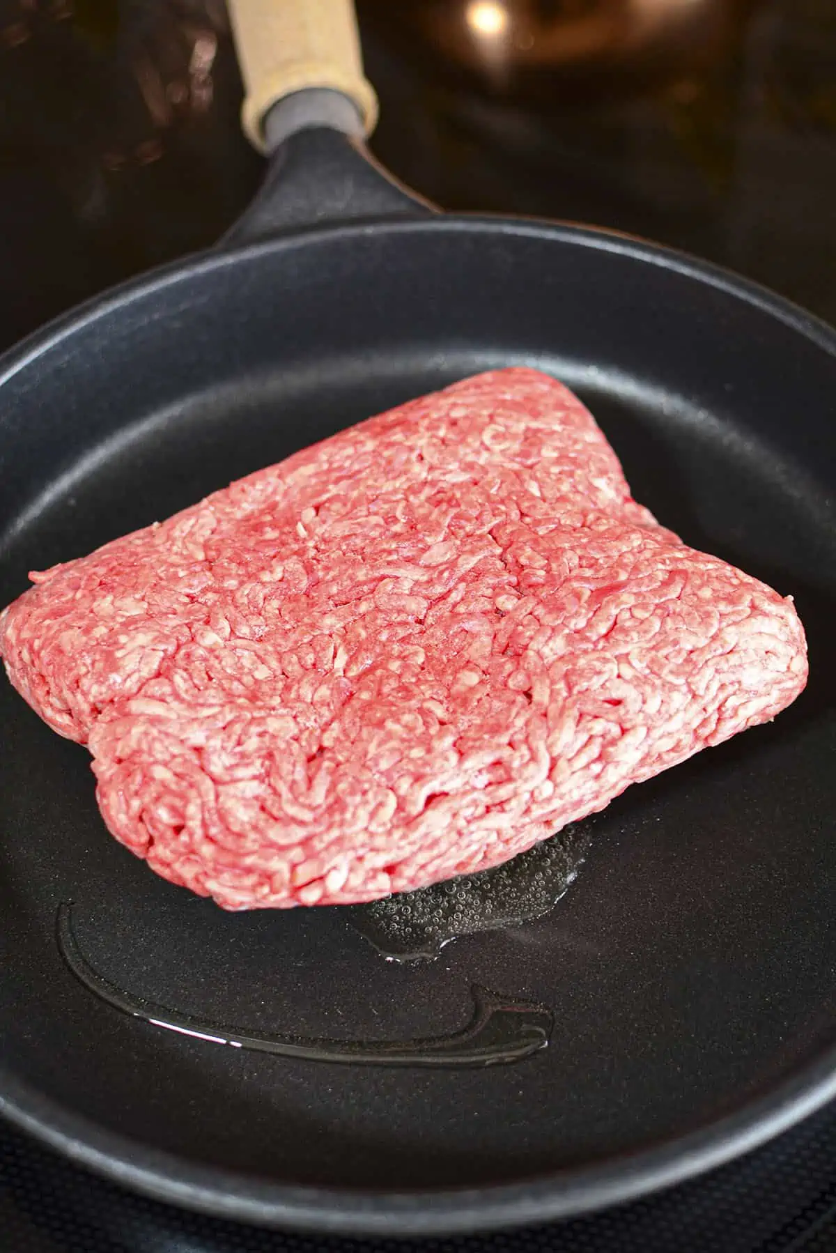 A frozen chunk of ground beef in a skillet with oil. 