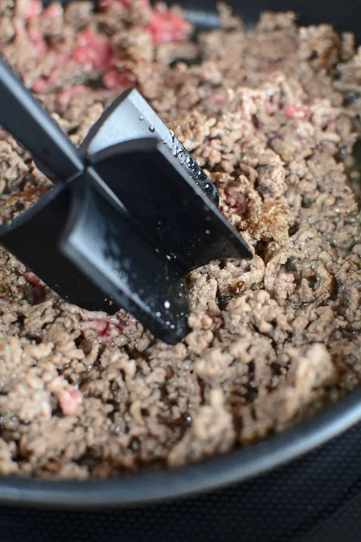 A meat chopper breaking up large ground beef crumbles.
