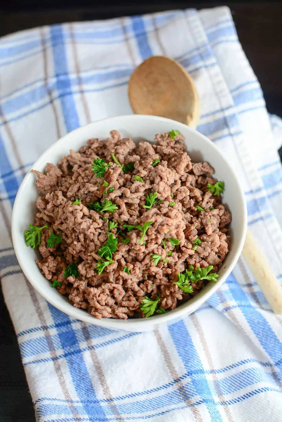 Cooked ground beef in a white bowl with a wooden spoon next to it.