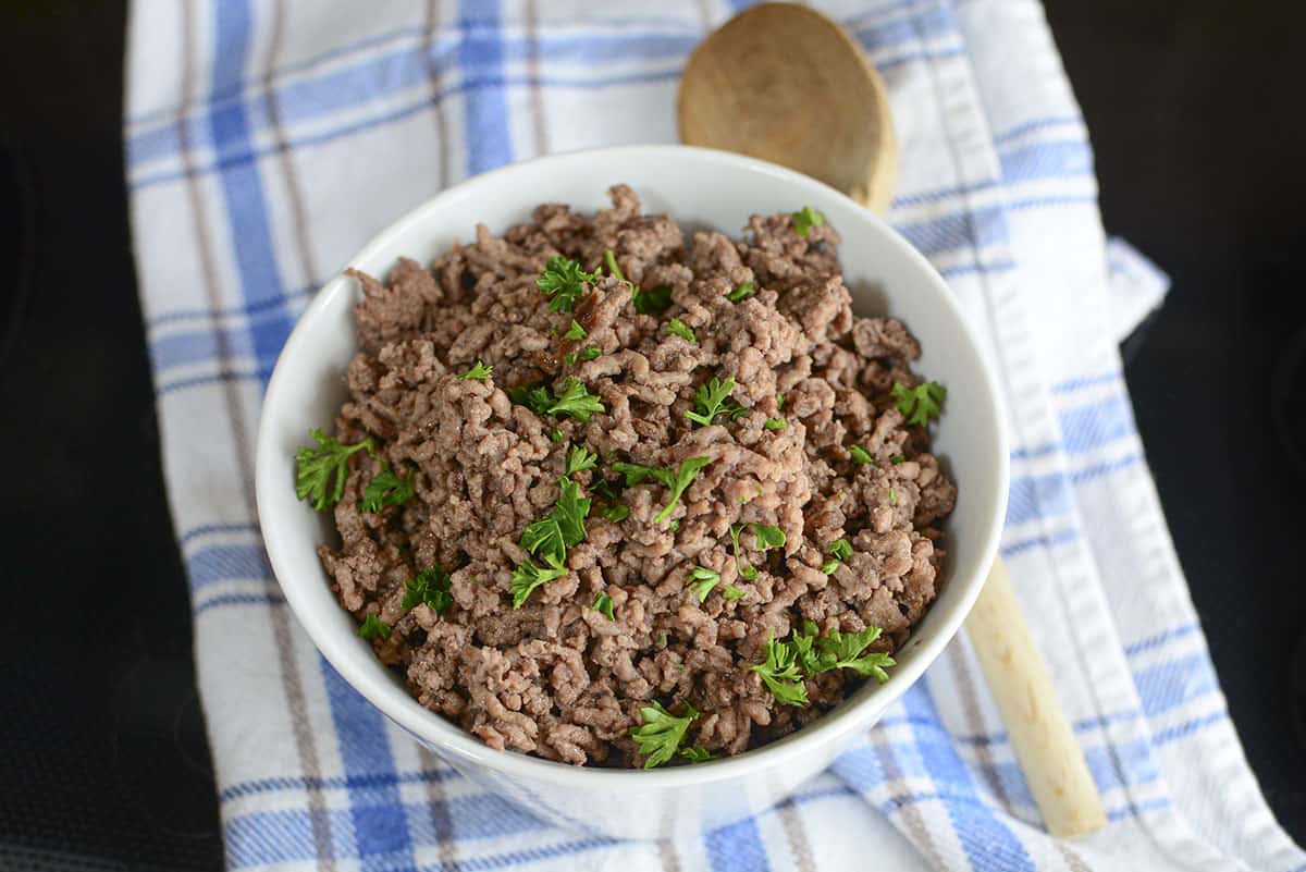 A bowl of cooked ground beef on a blue checked tea towel.
