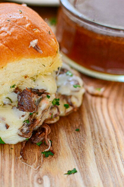 Roast beef slider with au jus dipping sauce on a wooden cutting board.