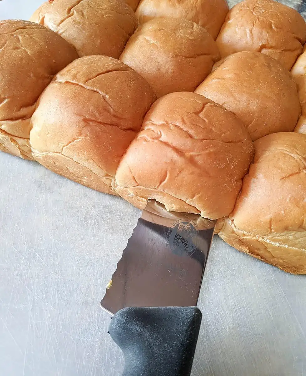 A knife cutting the tray buns in half horizontally.