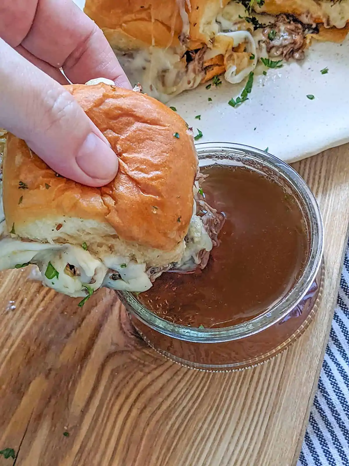 A roast beef slider with melted cheese being dunked into some au jus sauce.