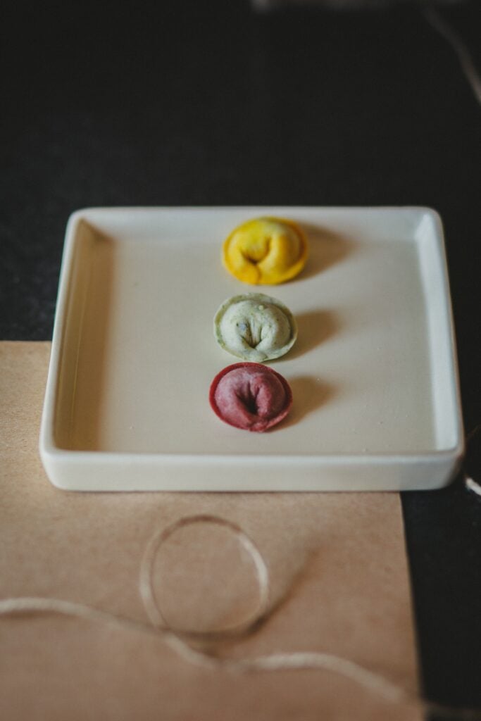 A photo of three tortellini on a plate. Yellow, green and red colored dough.