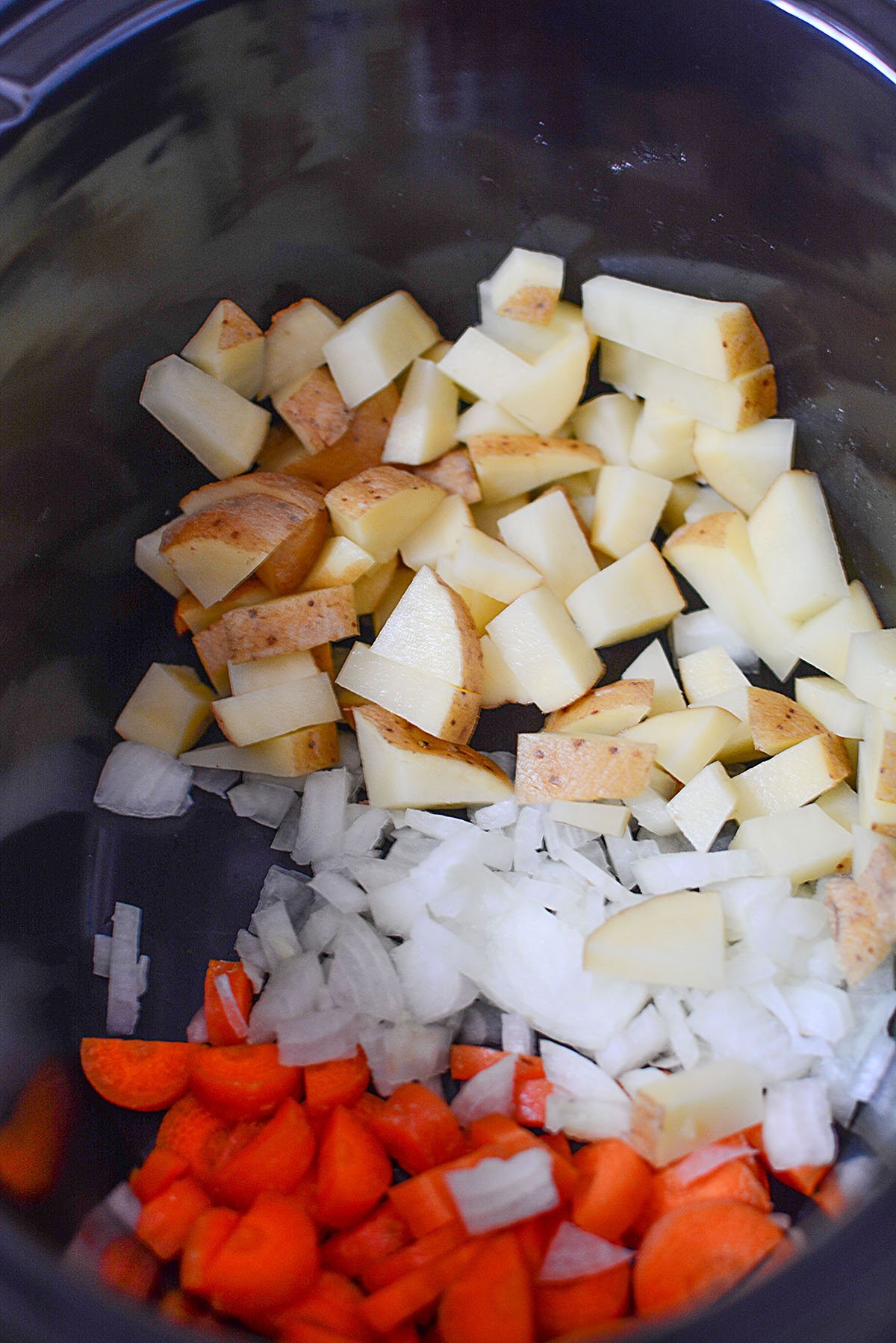 Potatoes, onions and carrots in a slow cooker bowl.