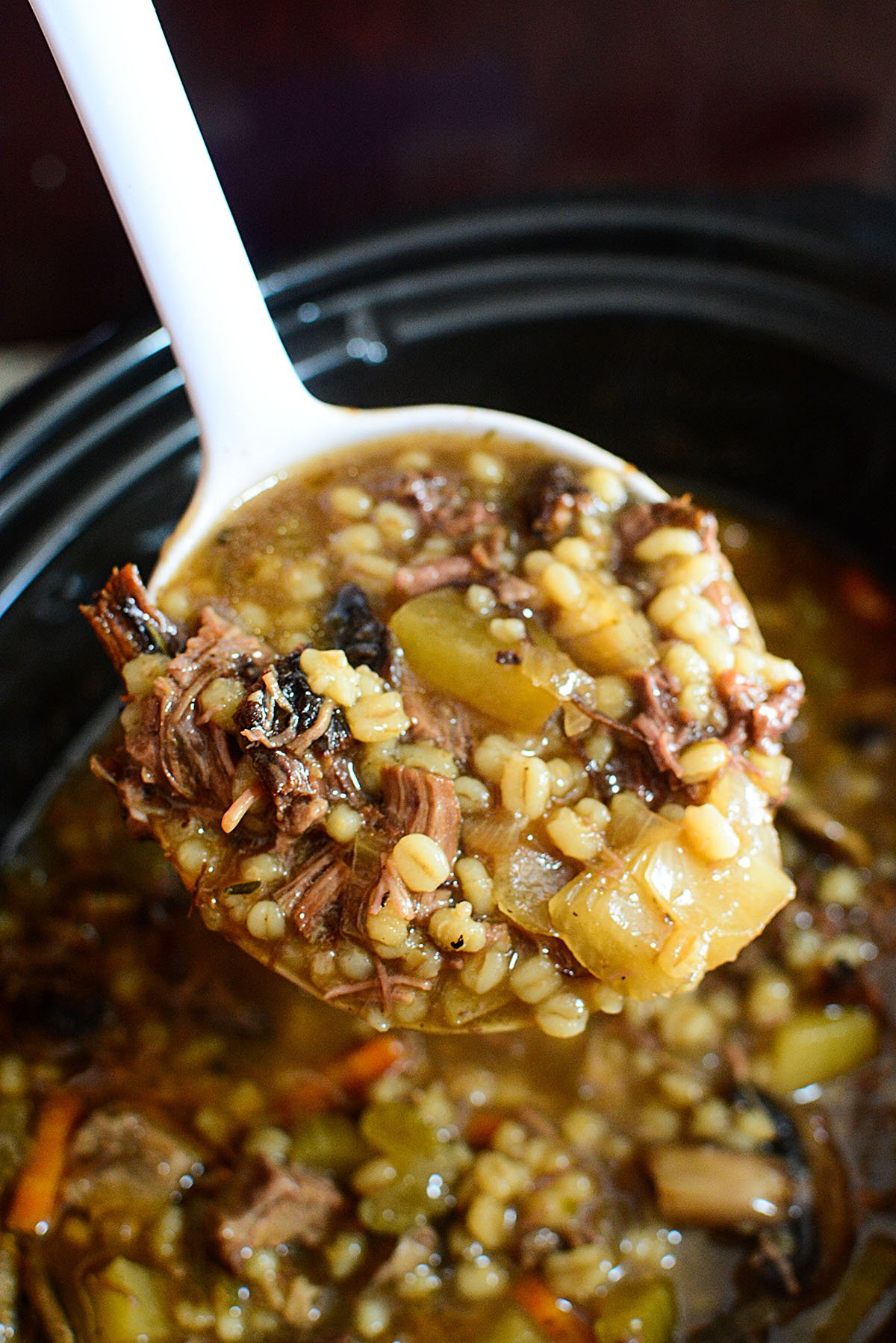 A white ladle portioning out beef and barley stew.