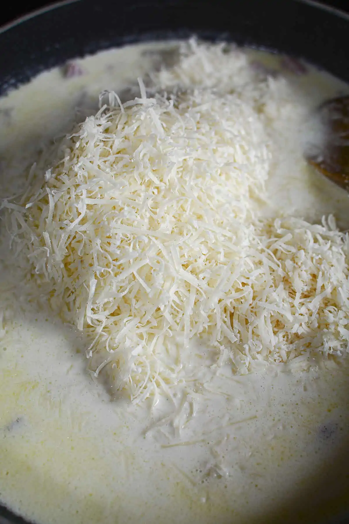 Grated parmesan cheese is melting into the cream sauce for the pasta dish.