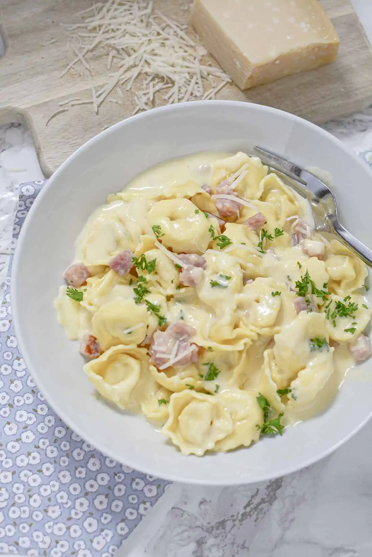 Tortellini and ham in a cream sauce in a white bowl. 