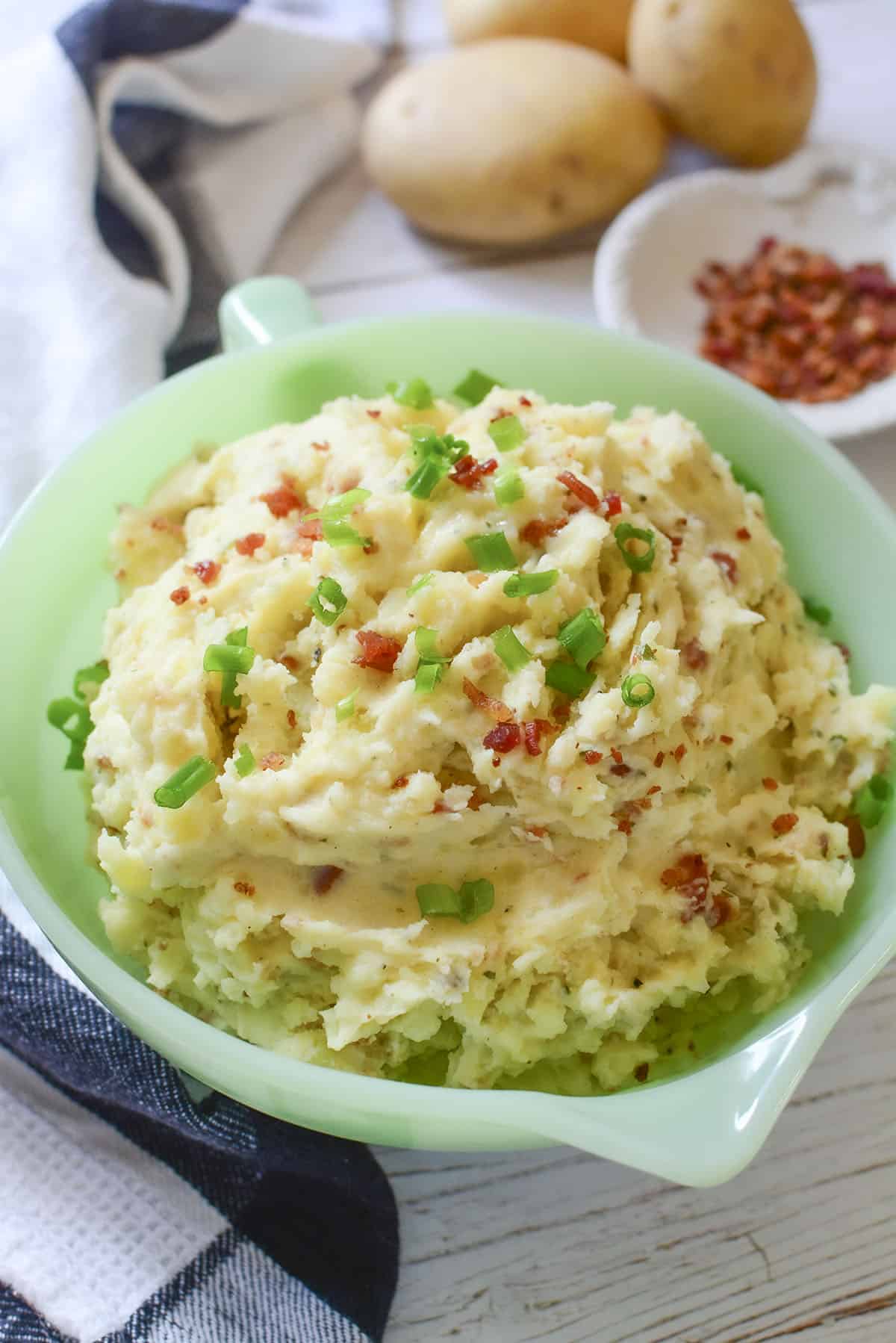 A close up photo of mashed potatoes with bacon bits and green onion sprinkled on top.