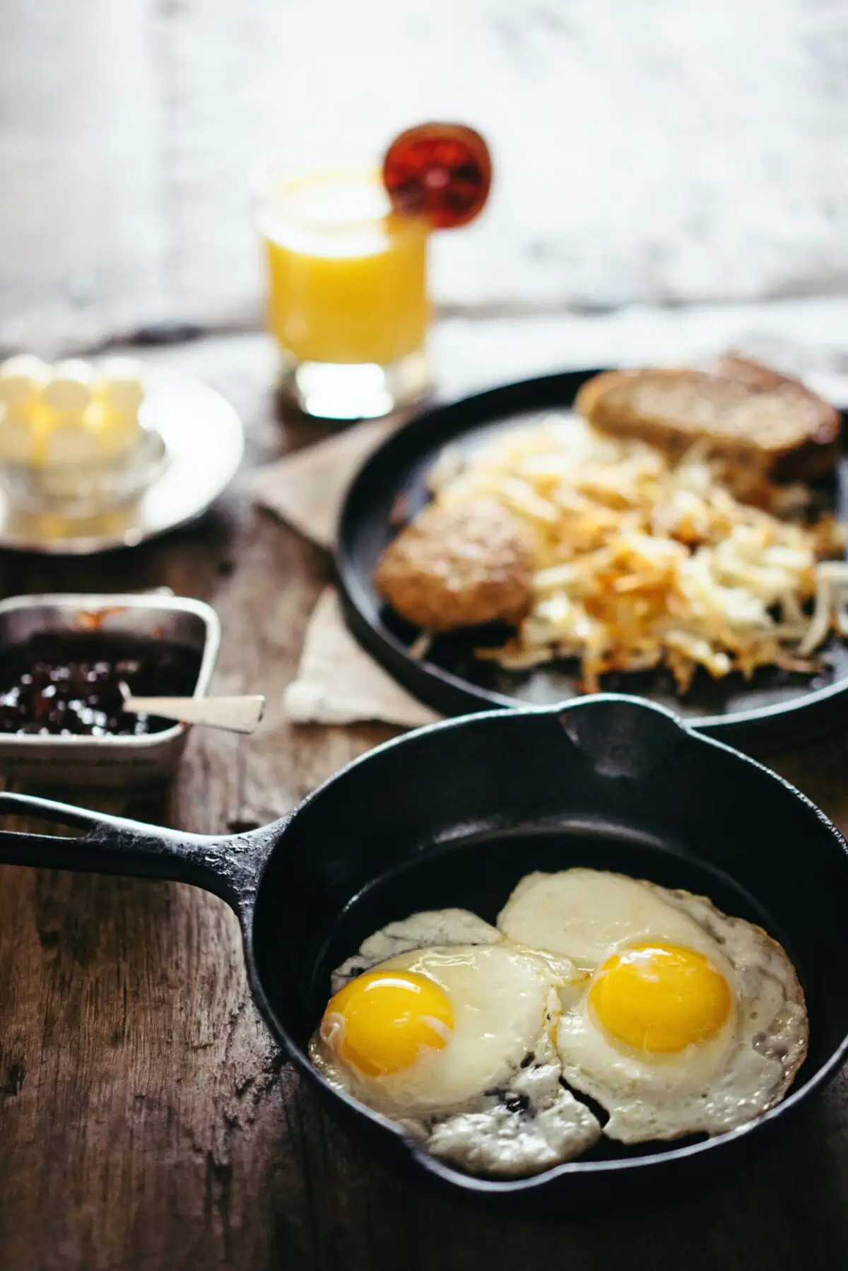 Eggs in a skillet with other breakfast items in an unfocused background.