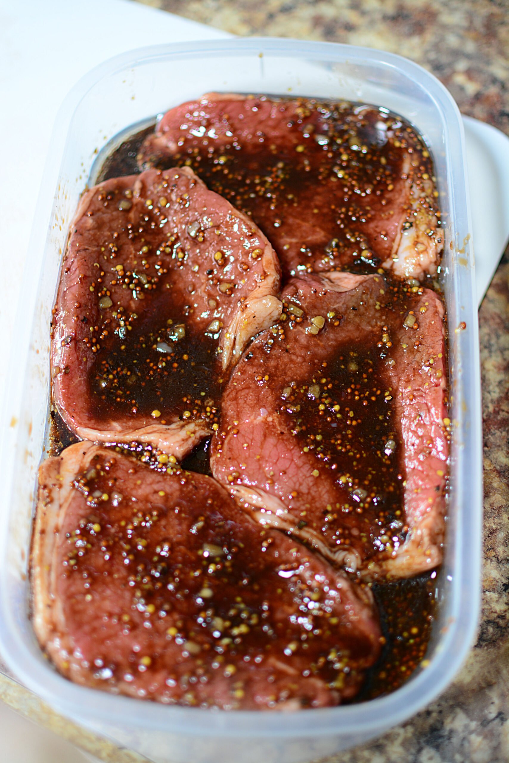 4 steaks infusing in a marinade in a container.