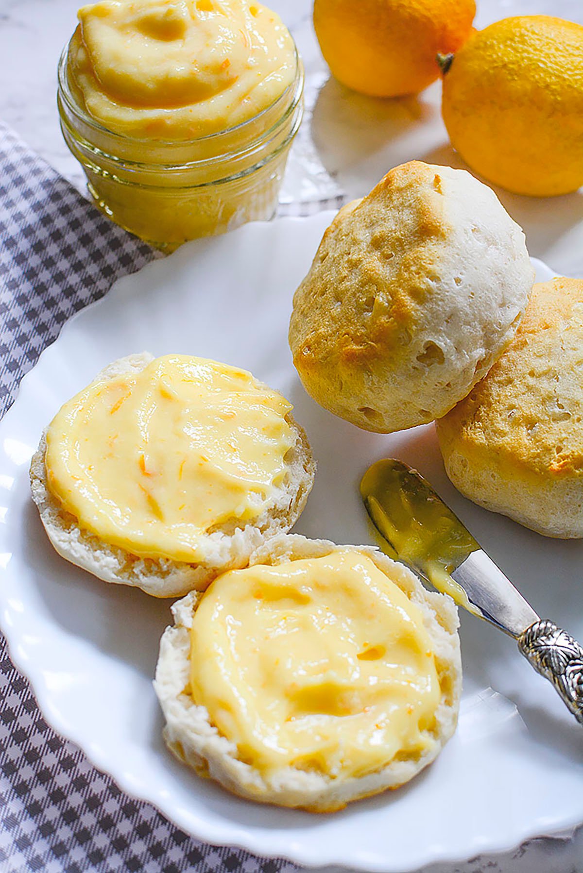 Meyer lemon curd spread on a biscuit with two other biscuits beside it and the glass container of curd above the plate.