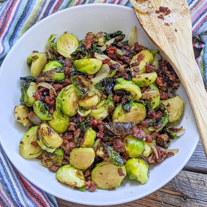 Cooked brussels sprounts with bacon and cranberries in a white bowl.