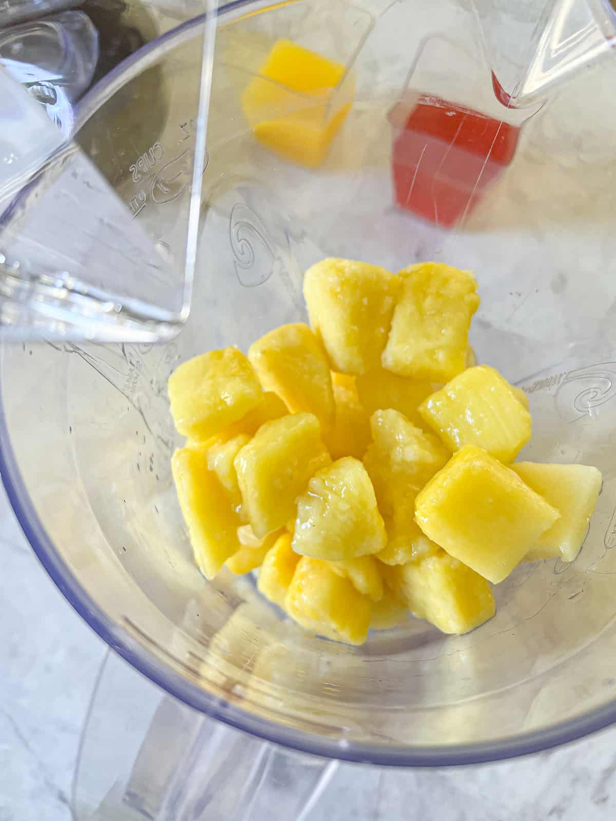 Pieces of frozen pineapple in the bottom of the blender with vodka mixed in.