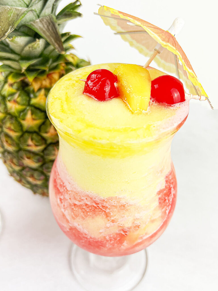 Pineapple slushie in a glass with two cherries on top.