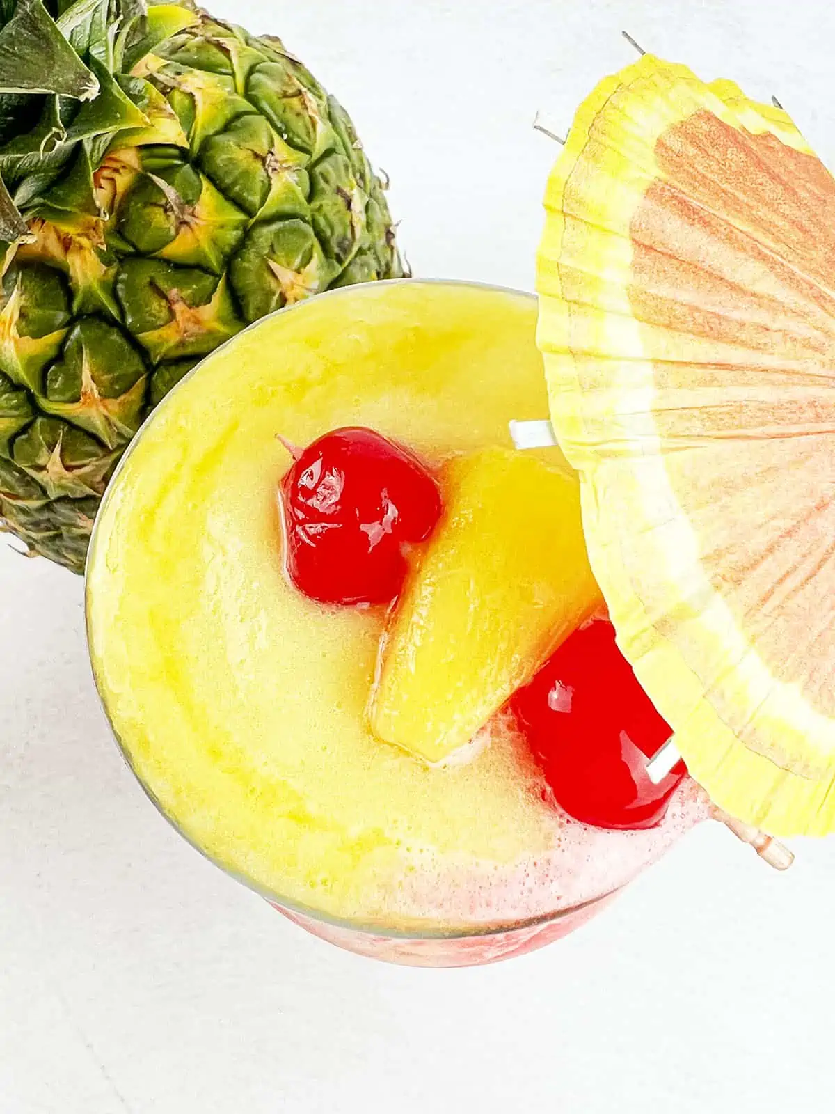 A top down image of the fruity slush drink with two cherries and a pineapple piece on top.