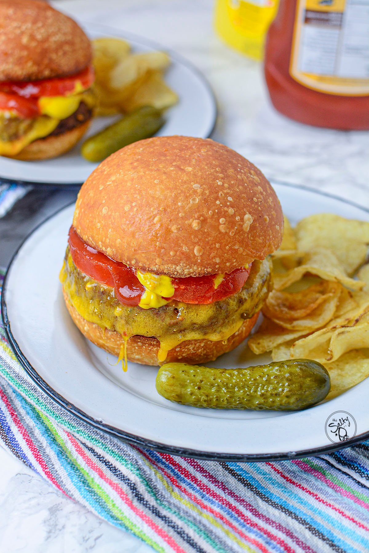 Two veggie burgers with cheese, pickles, tomatoes and condiments on white plates.