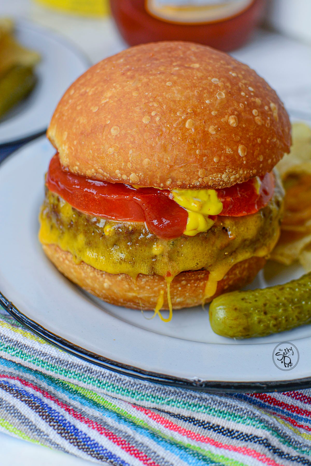 An air fryer veggie burger garnished with tomato, cheese, mustard and ketchup in a bun. 