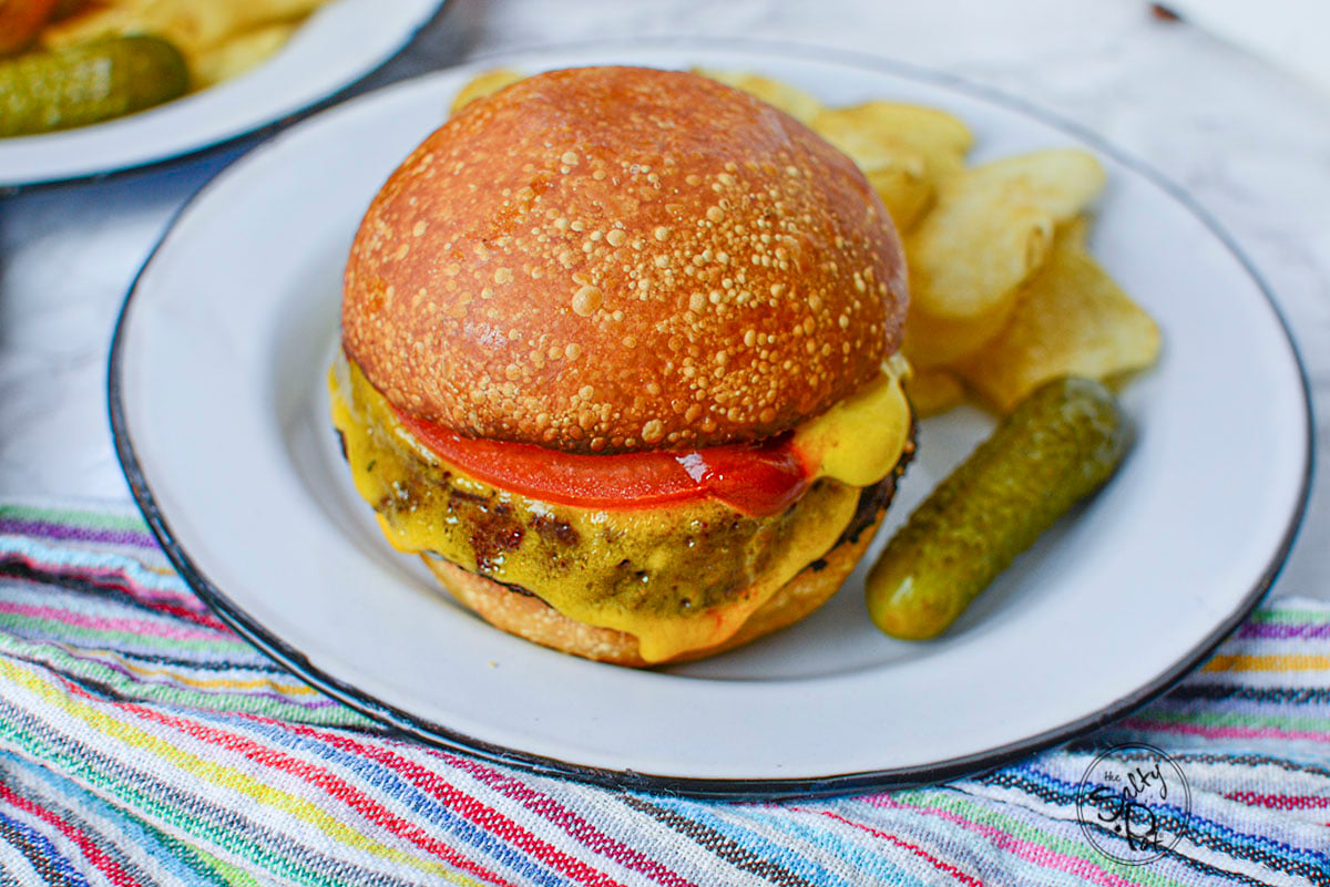 An alternative meat burger on a white plate with a pickle on the side.