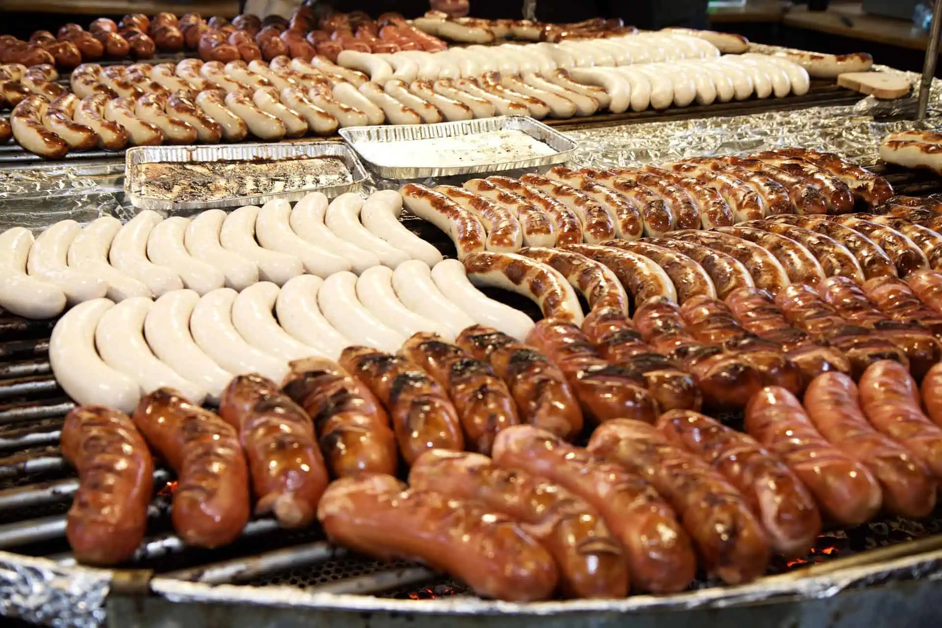 A variety of different brats on a large grill. 