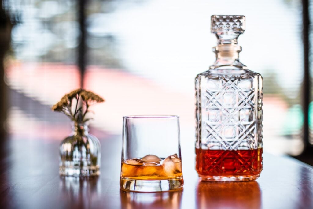 Alcohol in a decanter with a glass with ice sitting next to it.