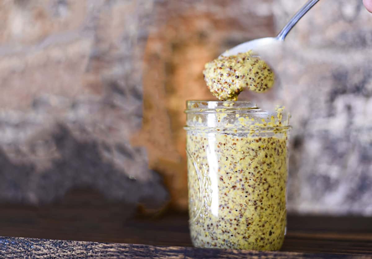 A spoon scooping out a dollop of stone ground mustard out of a jar.